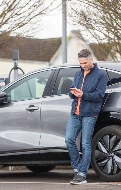 Supermarket charging - man leans against EV while using Zapmap on his phone