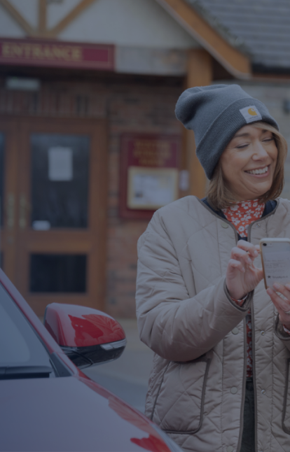 Two people looking at a phone screen with an electric car charging beside them