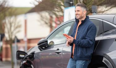 Man stands in front of charging EV while holding phone