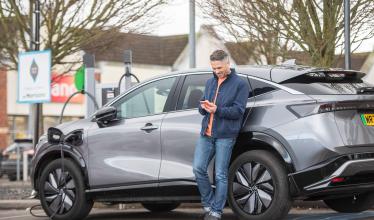 Supermarket charging - man leans against EV while using Zapmap on his phone
